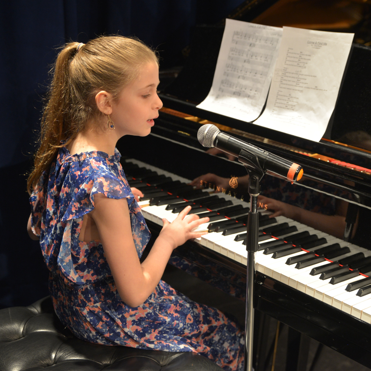 a young girl plays piano and sings her own song that she composed into a microphone