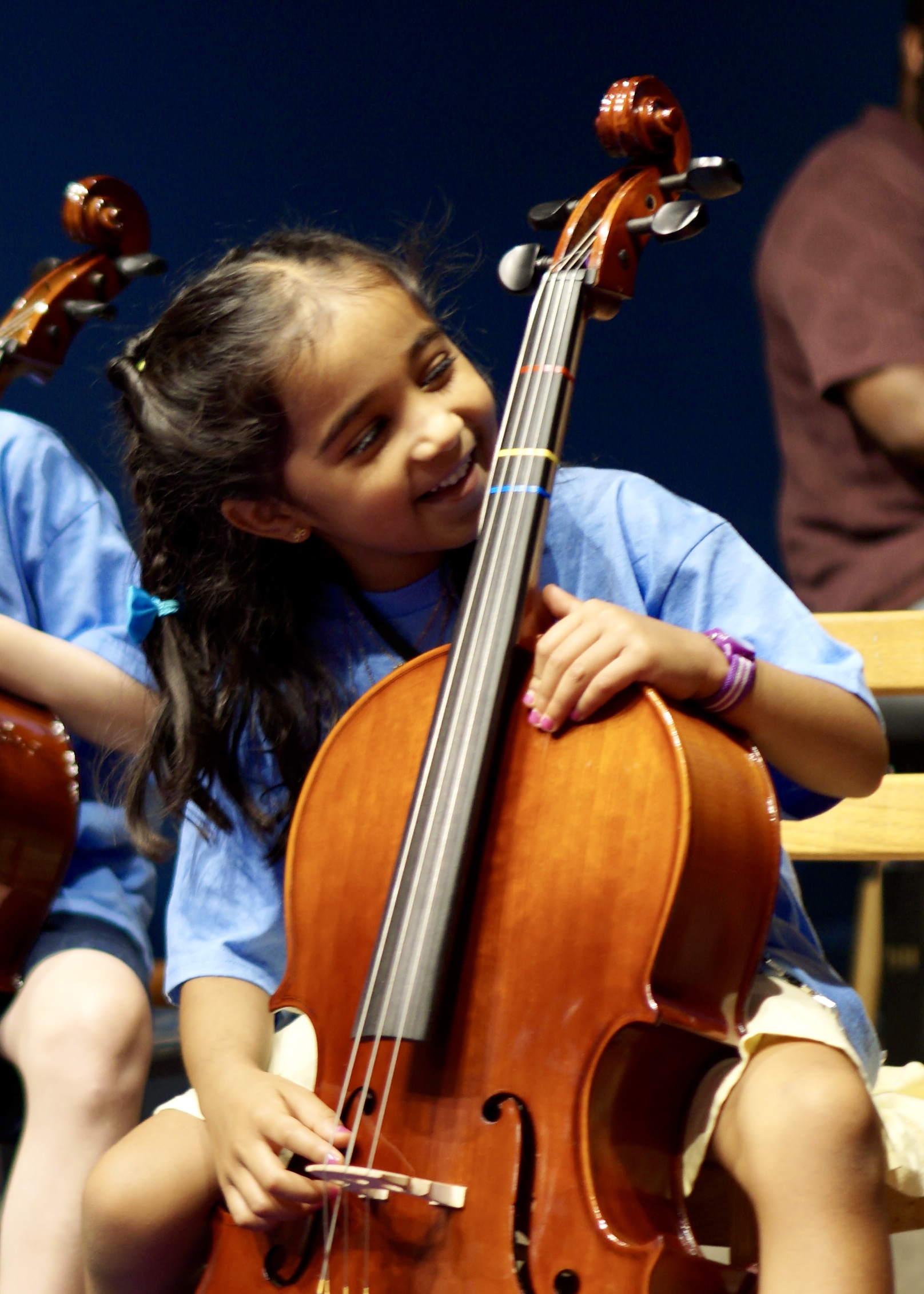 A smiling young cellist hugs her cello on stage during the Meet the Instruments Friday concert at Bloomingdale School of Music